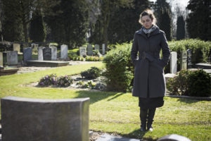 Woman sitting at grave with hands in pockets